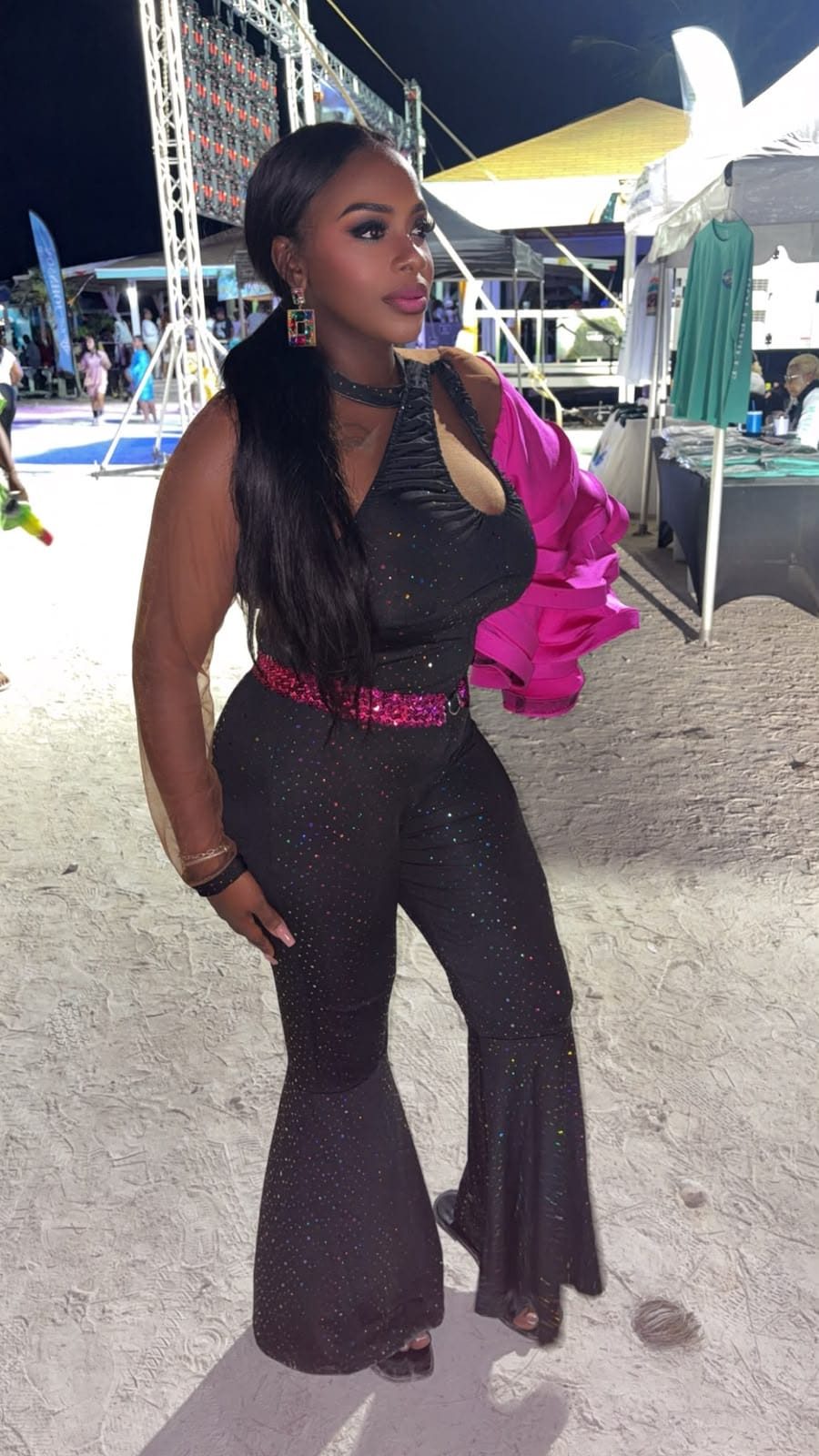 Mama D at a night festival in a black sparkling jumpsuit with a hot pink jacket over one shoulder