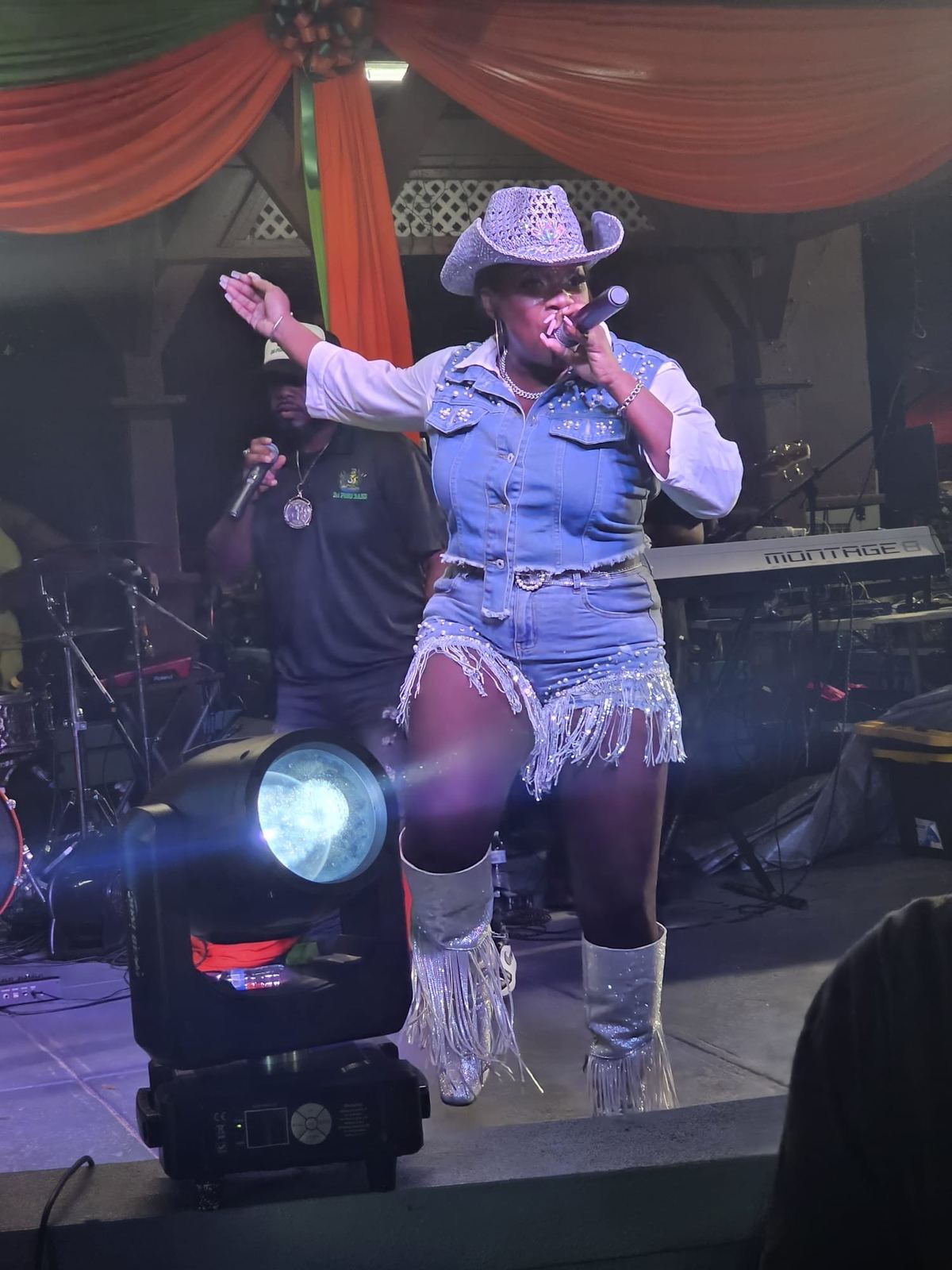 Mama D performing in a studded denim outfit, fringed shorts and a sequined cowboy hat