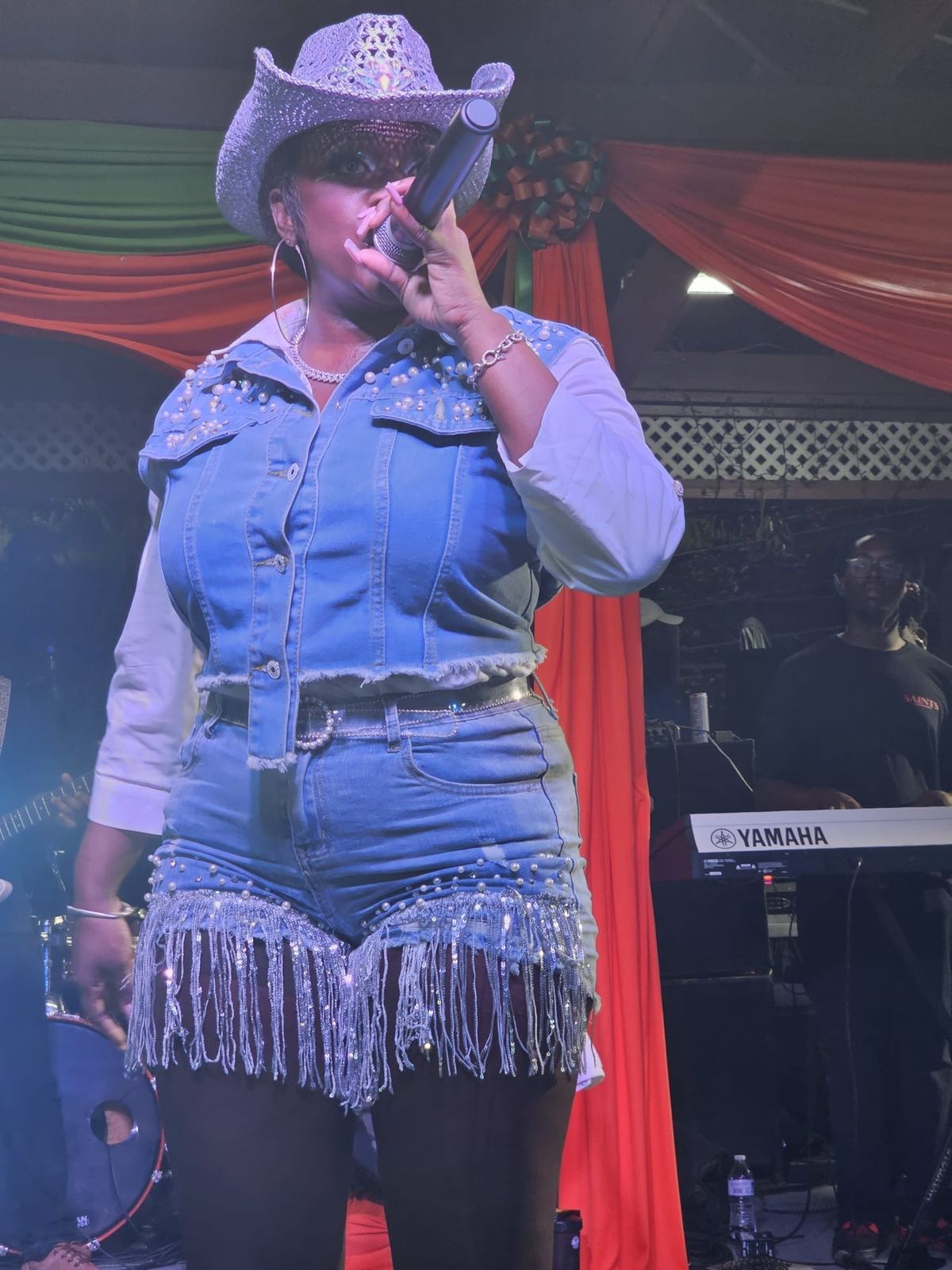 Close up of Mama D singing in a studded denim vest and sequined cowboy hat