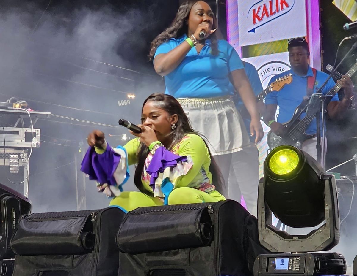 Mama D at the edge of the stage in a neon green outfit under a Kalik banner