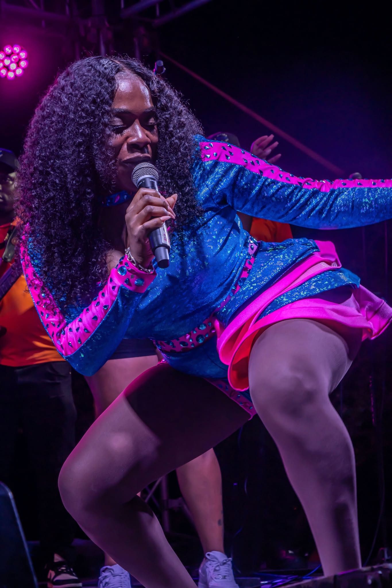 Mama D performing live under magenta and blue stage lights with her band behind her