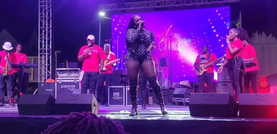 Wide shot of Mama D singing centre stage under purple lighting with a full band around her