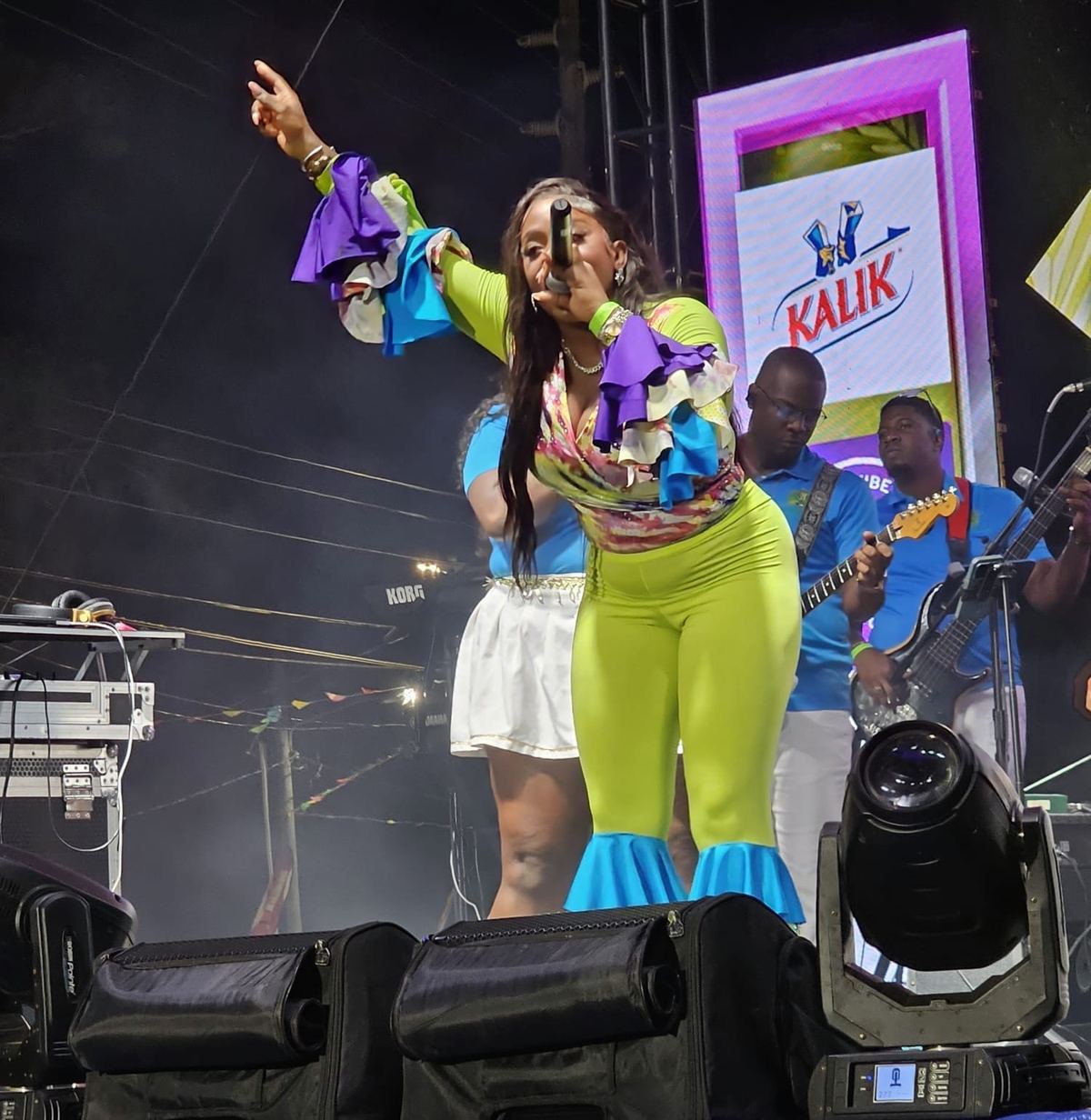Mama D with one arm raised singing on a Kalik sponsored stage