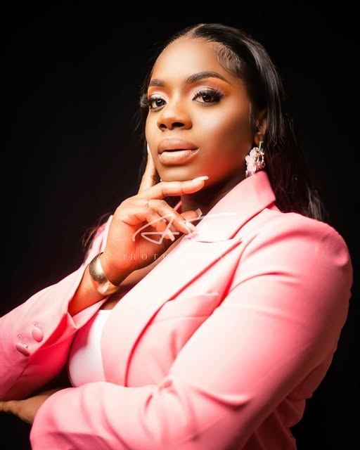 Studio portrait of Mama D in a pink blazer on a black backdrop