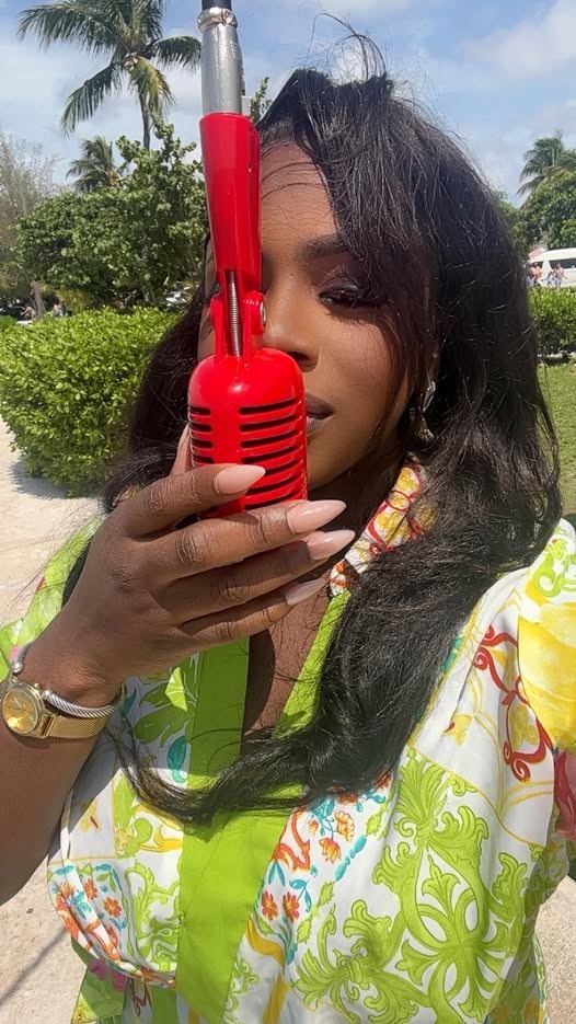 Mama D holding a red vintage style microphone in a bright printed shirt outdoors